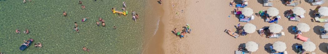 Spiaggia affollata, ombrelloni ordinati, mare limpido. Atmosfera estiva, gioia e relax ovunque.