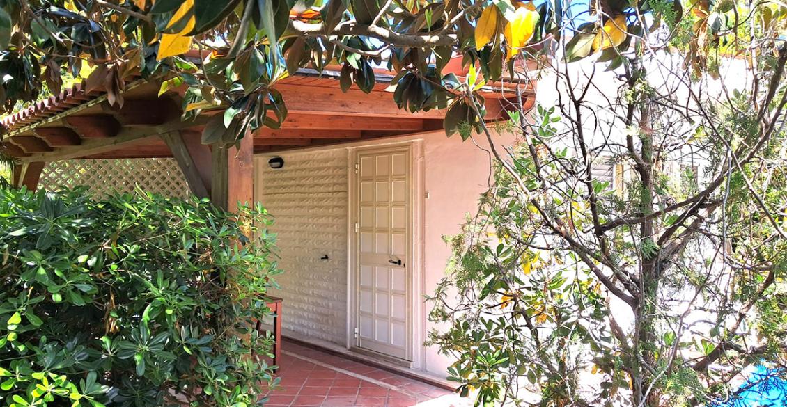 Veranda accogliente con tavolo in legno, circondata da piante verdi e luce solare calda.