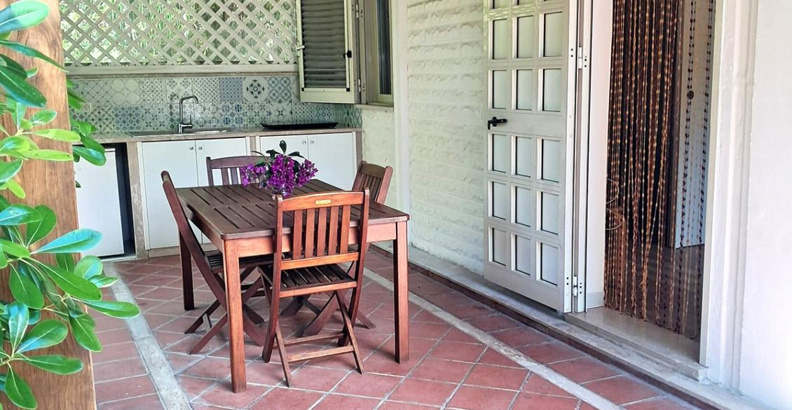 Cucina esterna accogliente, tavolo in legno, luce solare, atmosfera tranquilla e rilassante.