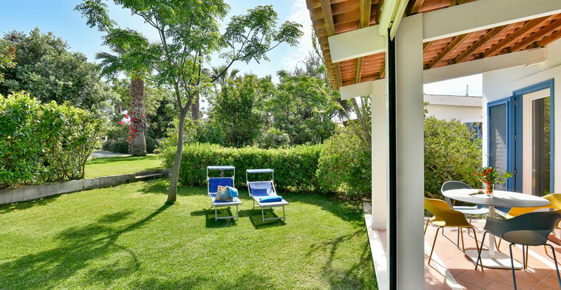 Giardino soleggiato con sedie a sdraio blu, veranda accogliente, fiori freschi e natura rigogliosa.