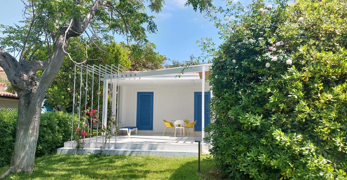 Casa bianca, finestre in legno, rampicante sul tetto, giardino verde, atmosfera accogliente e serena.