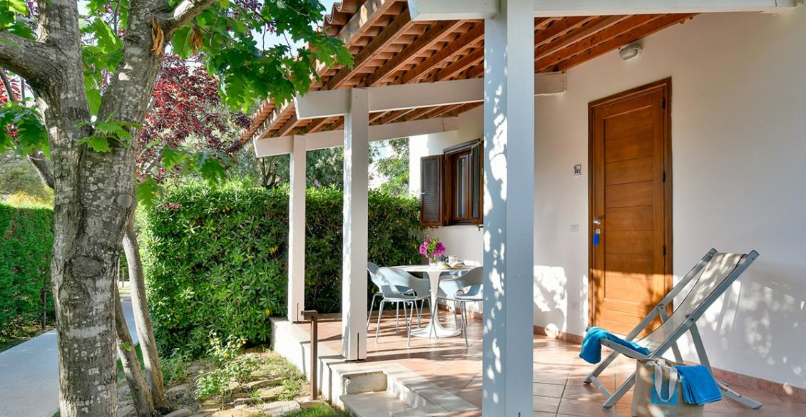 Piccolo bungalow bianco, immerso nel verde, con veranda accogliente e giardino curato.