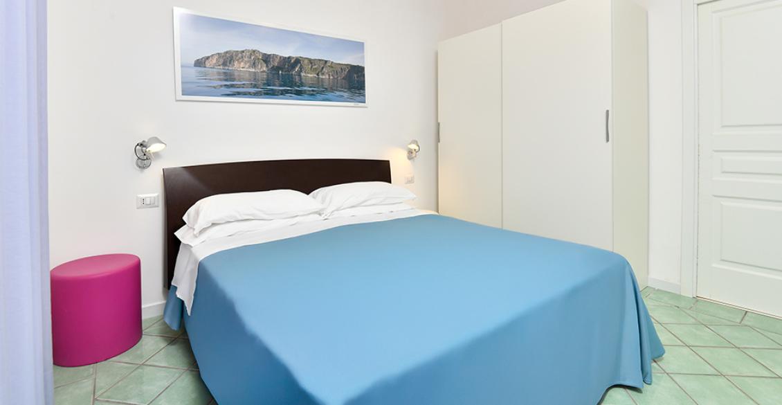 Cucina luminosa con mobili rossi, tavolo bianco e divano blu, atmosfera accogliente e moderna.
