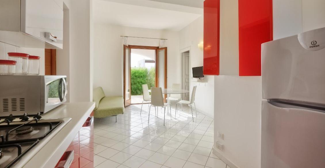 Cucina luminosa, moderna, con dettagli rossi, tavolo tondo e porta verso il giardino.