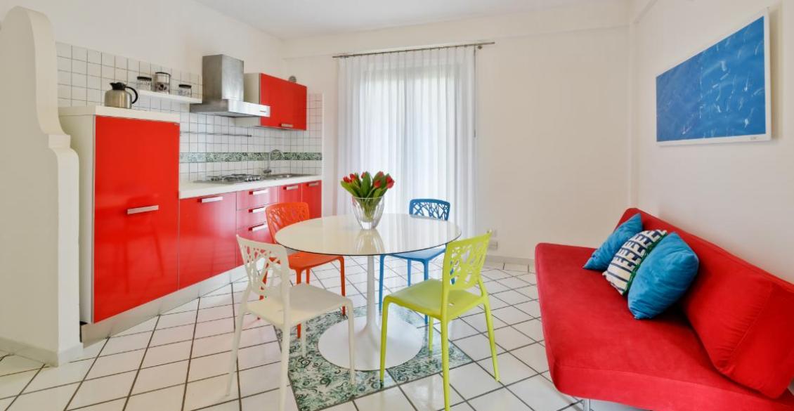 Cucina vivace con mobili rossi, sedie colorate e atmosfera luminosa e moderna.
