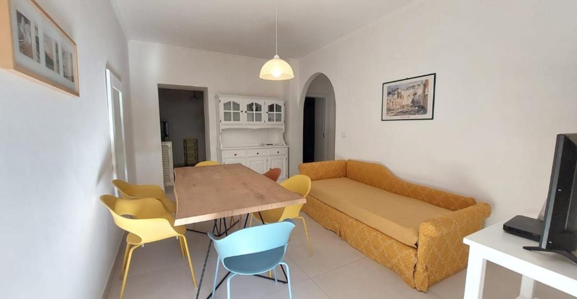 Sala accogliente con tavolo in legno, sedie colorate e divano giallo, atmosfera luminosa.