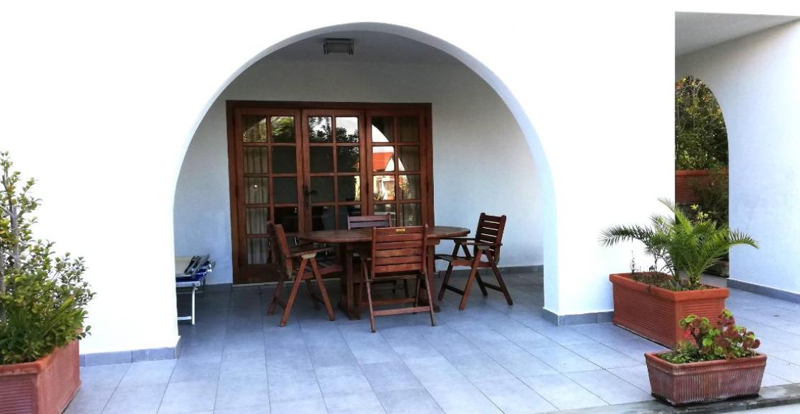 Veranda accogliente con tavolo in legno, sedie e piante in vasi, atmosfera rilassante.