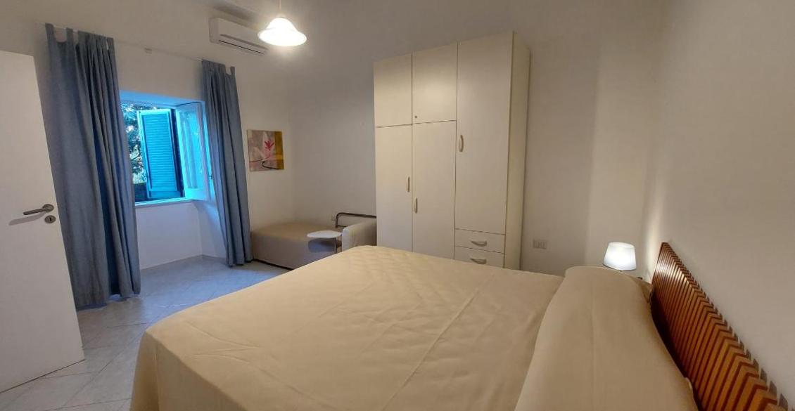 Camera accogliente con letto matrimoniale, armadio bianco, luce soffusa e finestra aperta.