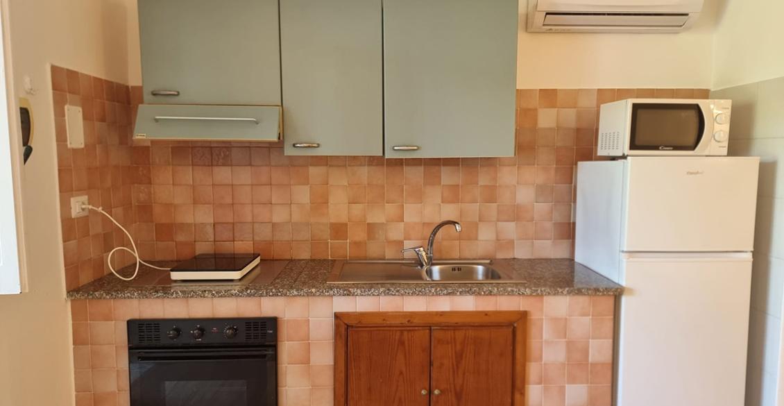 Cucina compatta con piastrelle calde, elettrodomestici essenziali e un'atmosfera accogliente e funzionale.