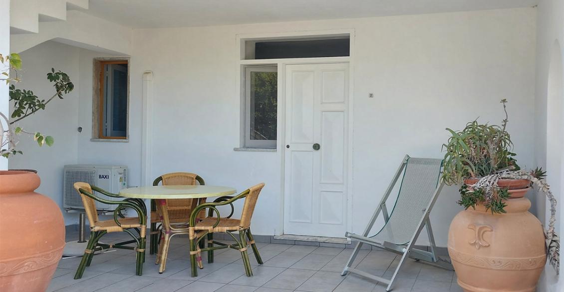 Veranda luminosa con tavolo, sedie intrecciate e piante in grandi vasi di terracotta.
