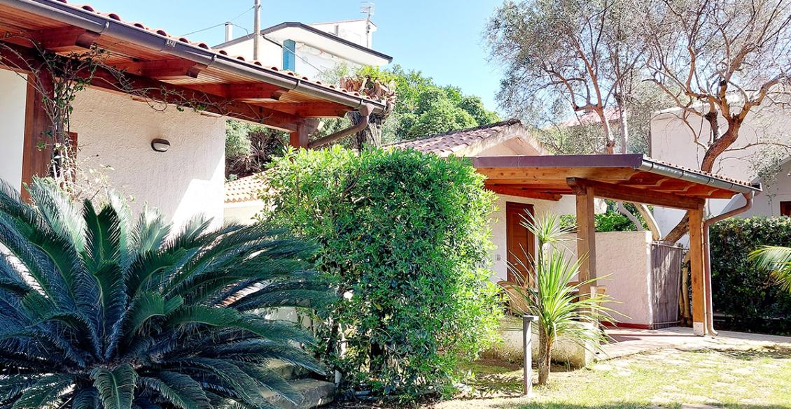 Veranda accogliente con tavolo, sedie bianche, piante verdi e tetto in legno.