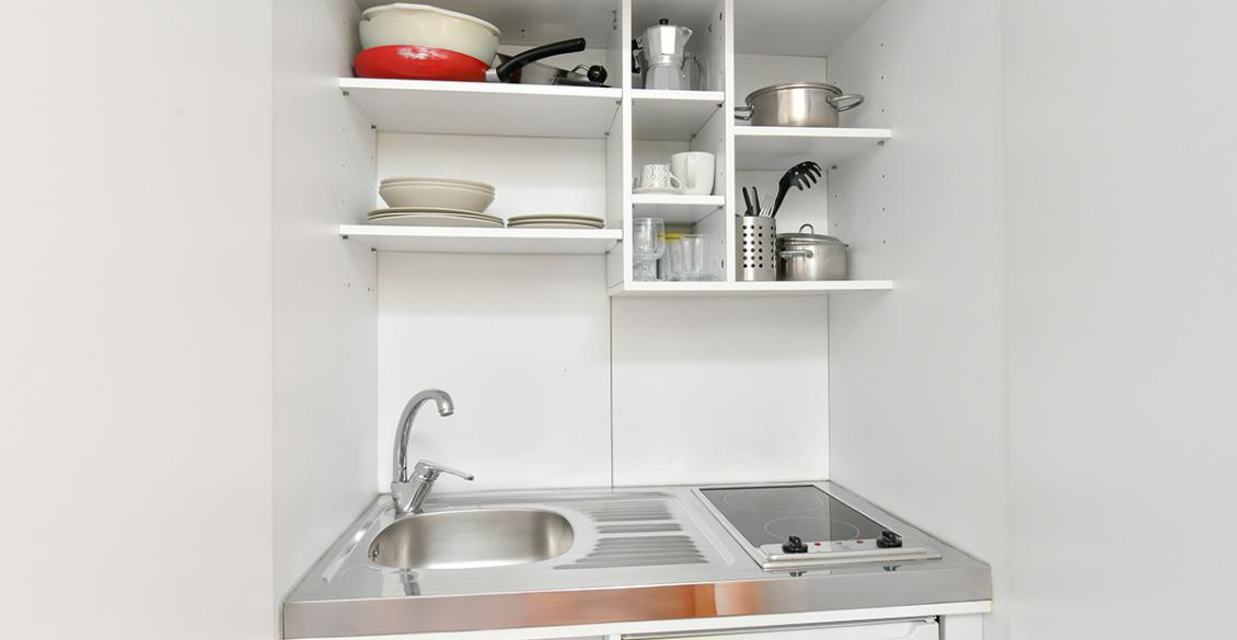 Piccola cucina accogliente, piatti ordinati, fornello e lavandino in legno chiaro.