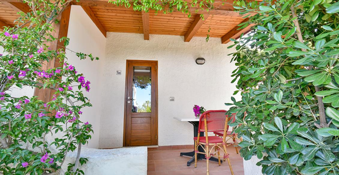 Veranda accogliente con tavolo, sedie bianche, piante verdi e tetto in legno.