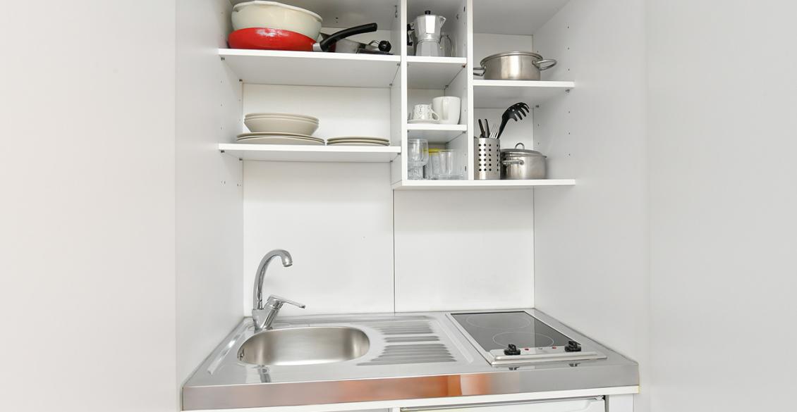 Cucina compatta e ordinata, piatti bianchi, lavello e fornello, atmosfera accogliente e funzionale.