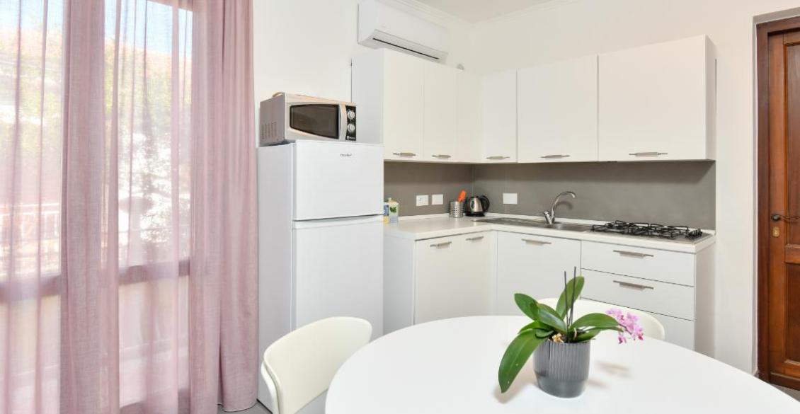 Cucina luminosa e moderna, con tenda rosa e pianta su tavolo bianco.