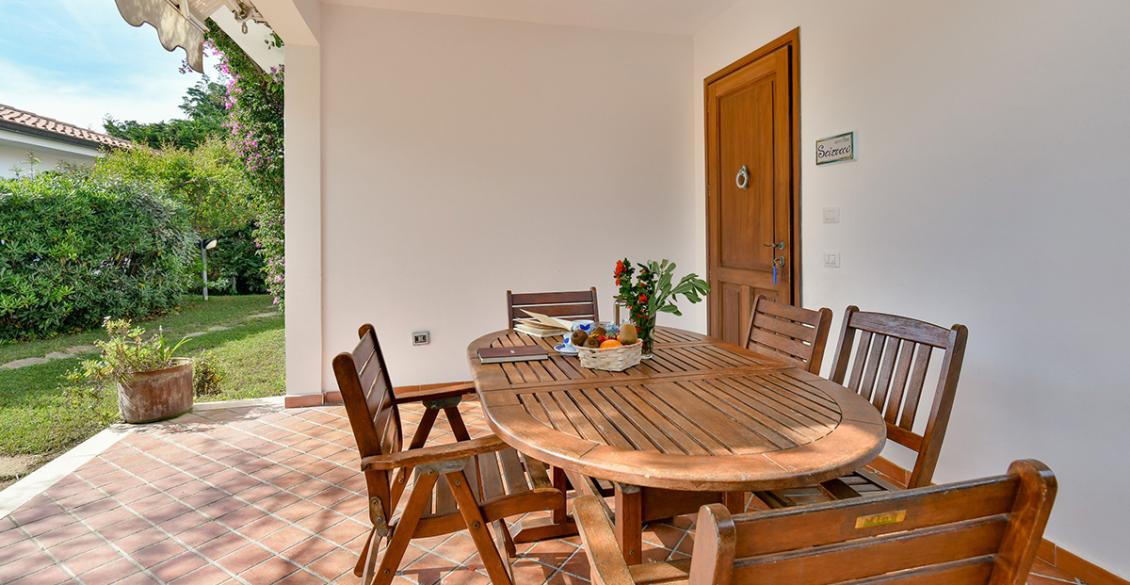 Terrazza accogliente con tavolo in legno, circondata da verde rigoglioso e luce solare.