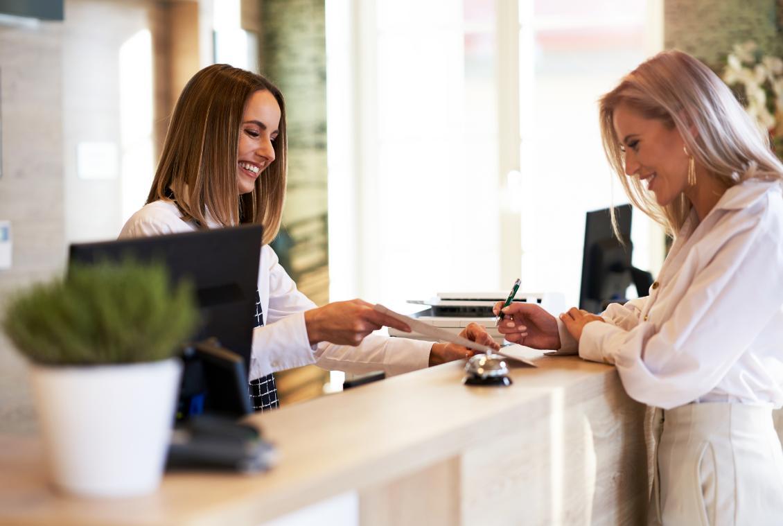 Due donne sorridono al banco reception, trasmettono accoglienza e cordialità.