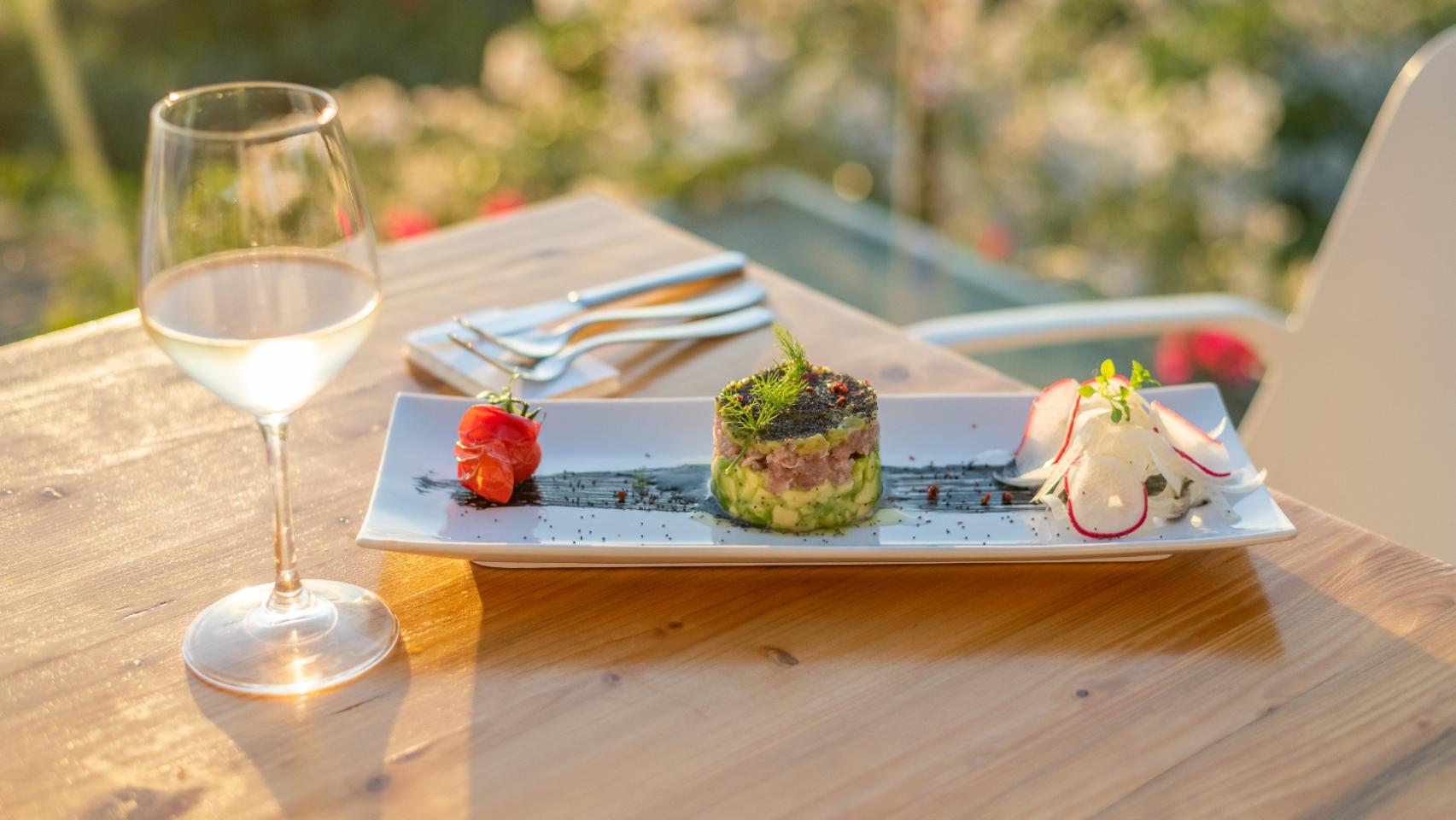 Piatto elegante con tartare, pomodoro, ravanelli e bicchiere di vino al tramonto.
