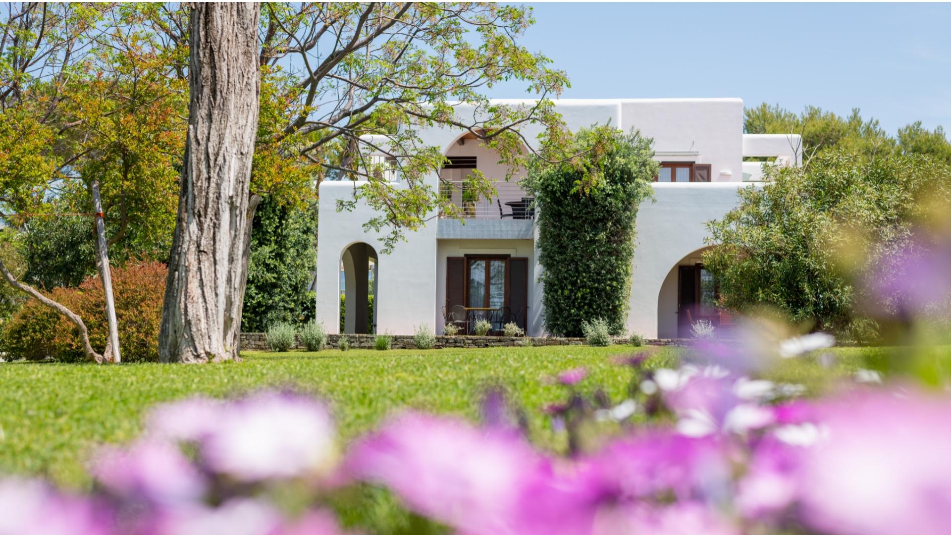 Casa bianca immersa nel verde con fiori colorati in primo piano.