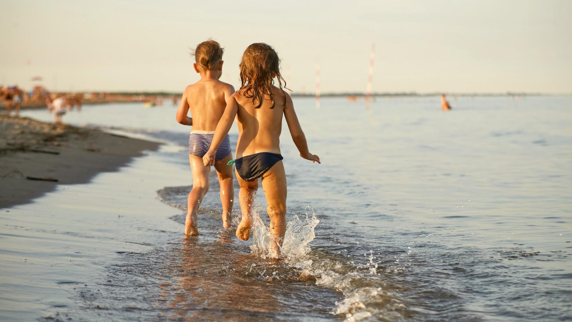 Due bambini corrono felici sulla spiaggia, spruzzi d'acqua e sole caldo.