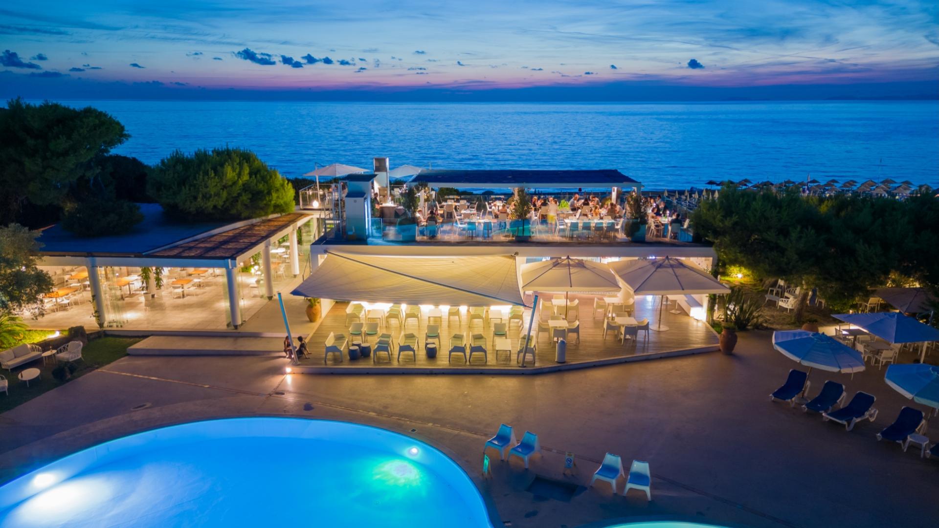 Tramonto sul mare, ristorante elegante, atmosfera rilassante e piscina illuminata, perfetta armonia.