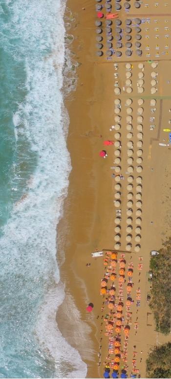 Vista aerea di spiaggia, ombrelloni colorati, onde e piscina in un resort estivo.
