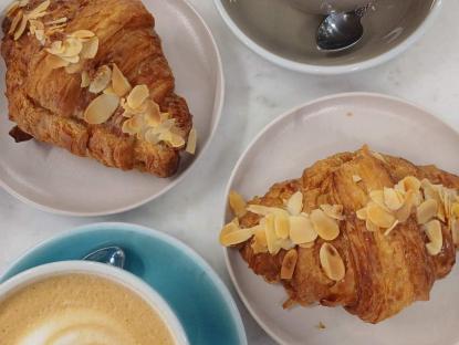 Due croissant dorati con mandorle affettate, su piatti bianchi, evocano calore e dolcezza.