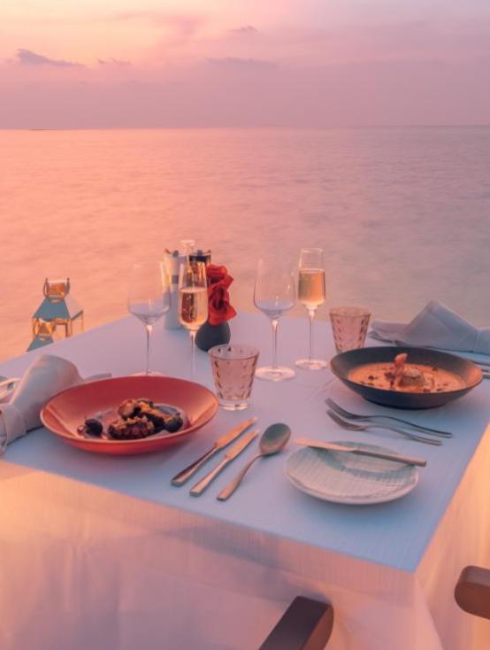 Cena romantica al tramonto sul mare, tavola elegante, atmosfera intima e serena.