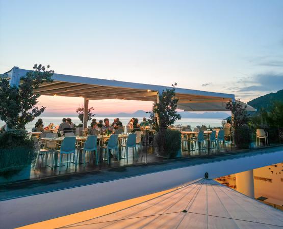 Terrazza sul mare, sedie bianche, sole caldo, vista mozzafiato, atmosfera rilassante e tranquilla.