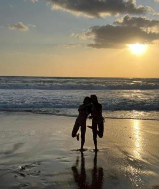 Due persone abbracciate sulla spiaggia al tramonto, onde e sole creano un'atmosfera magica.