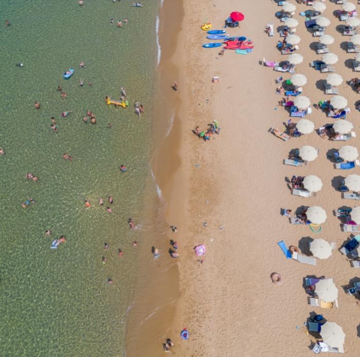Spiaggia affollata, ombrelloni ordinati, mare cristallino, estate vivace, gioia e relax.