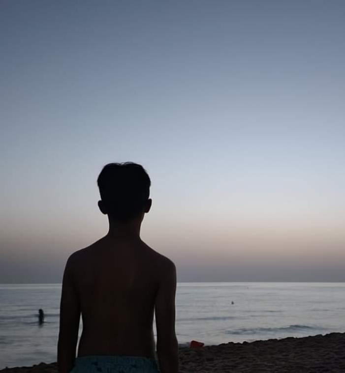 Un ragazzo osserva il mare al tramonto, evocando pace e contemplazione silenziosa.