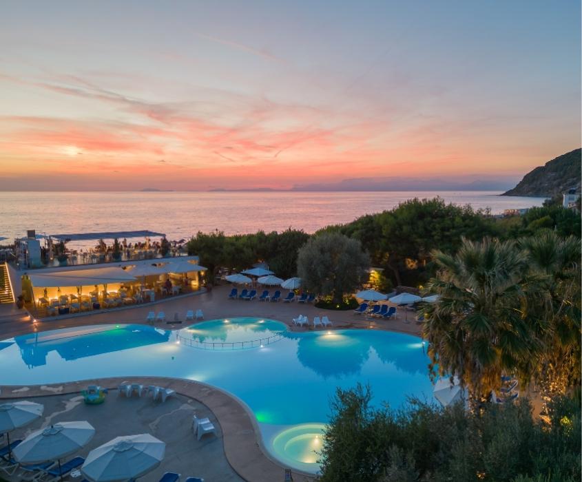 Tramonto mozzafiato su piscina e mare, atmosfera rilassante e accogliente, colori caldi e vivaci.