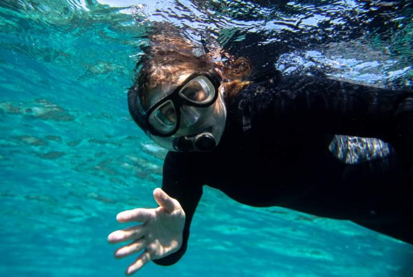 Una persona nuota sott'acqua con maschera, immersa in un mare cristallino e avvolgente.